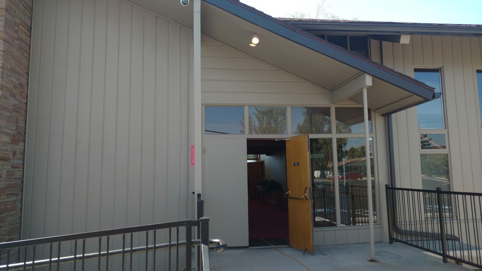 The entrance to a building with beige vertical wood siding, a partial glass facade, and a slightly open wooden door.