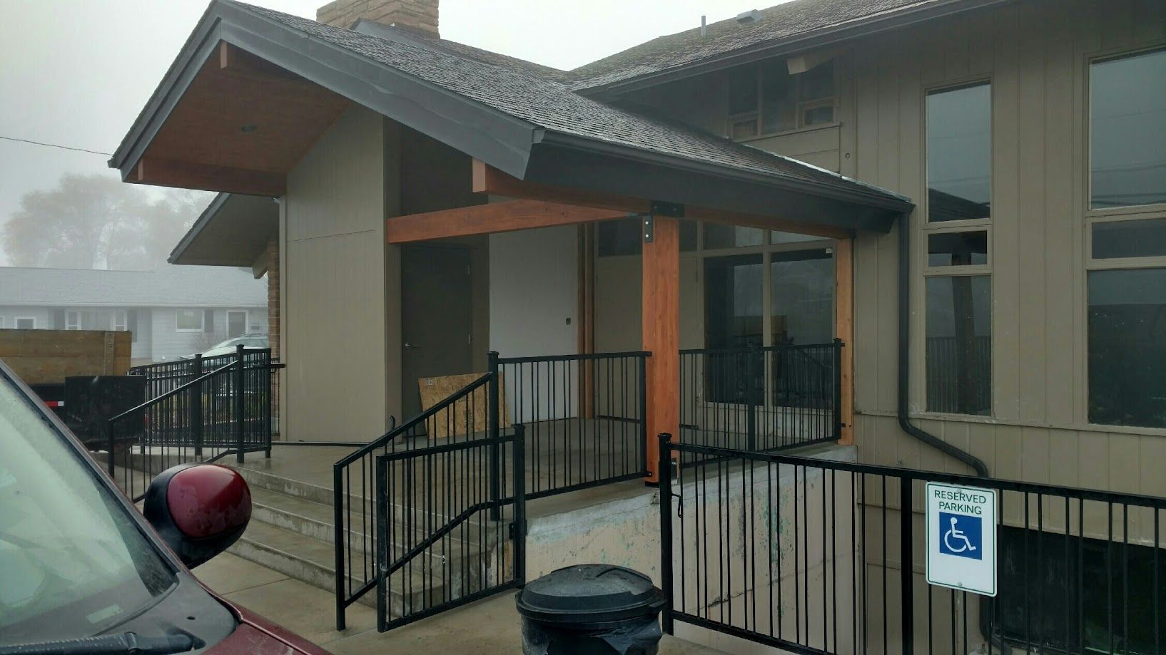A beige building entrance with a covered porch, black railings, stairs, and an accessible parking sign.