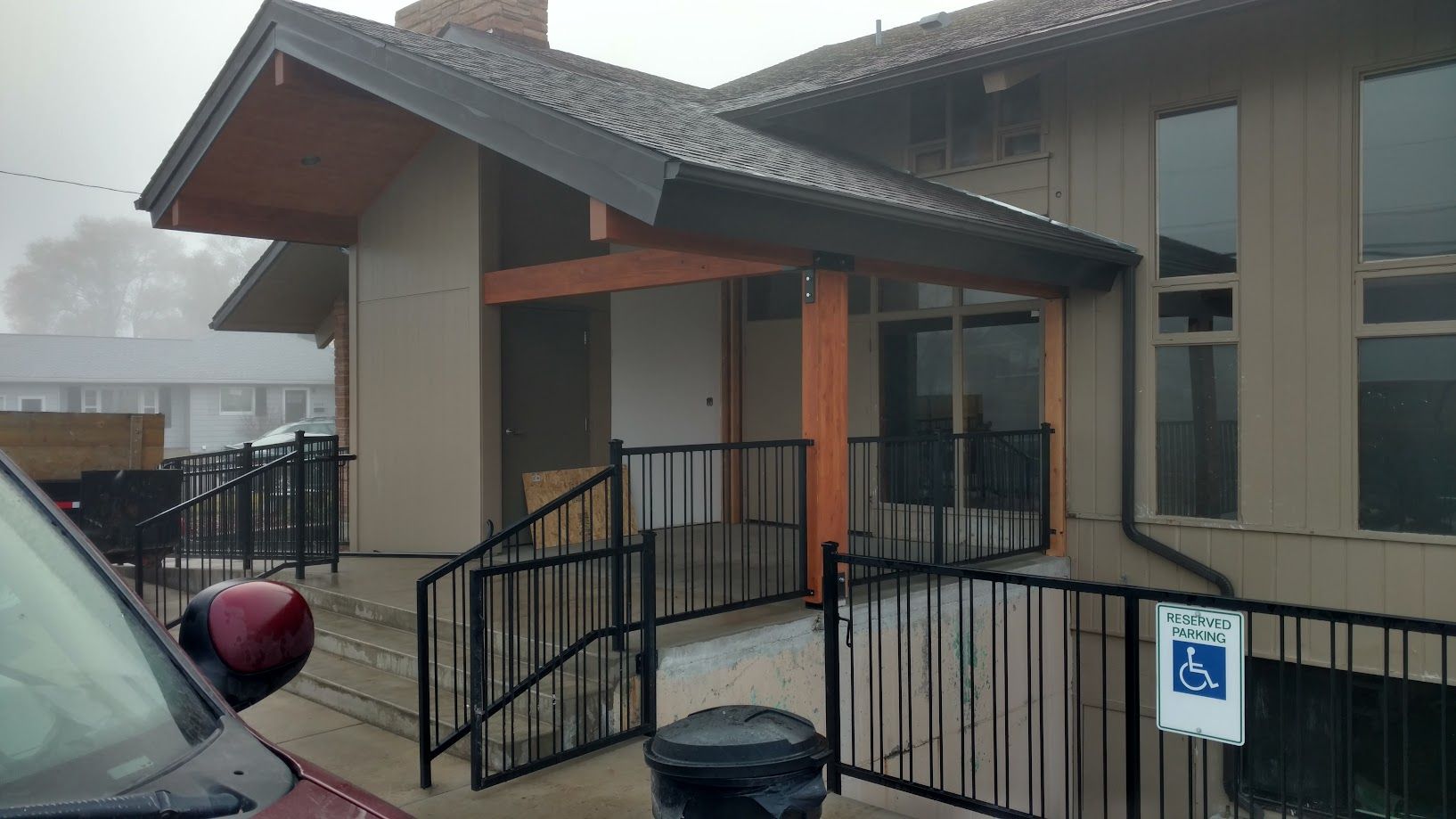 A brown building entrance with a black metal handrail leading to a ramp, featuring a blue handicap parking sign.