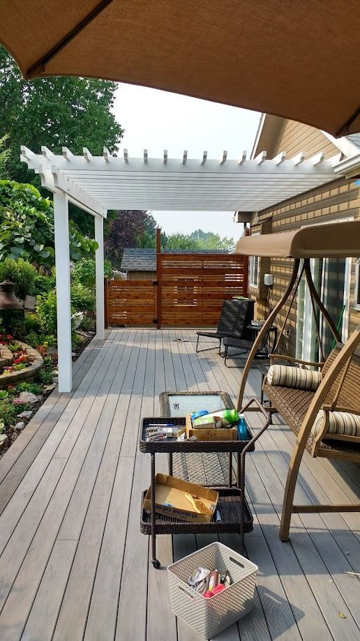 A wooden deck with a white pergola, a hanging porch swing, a rolling utility cart, and a wooden privacy screen.