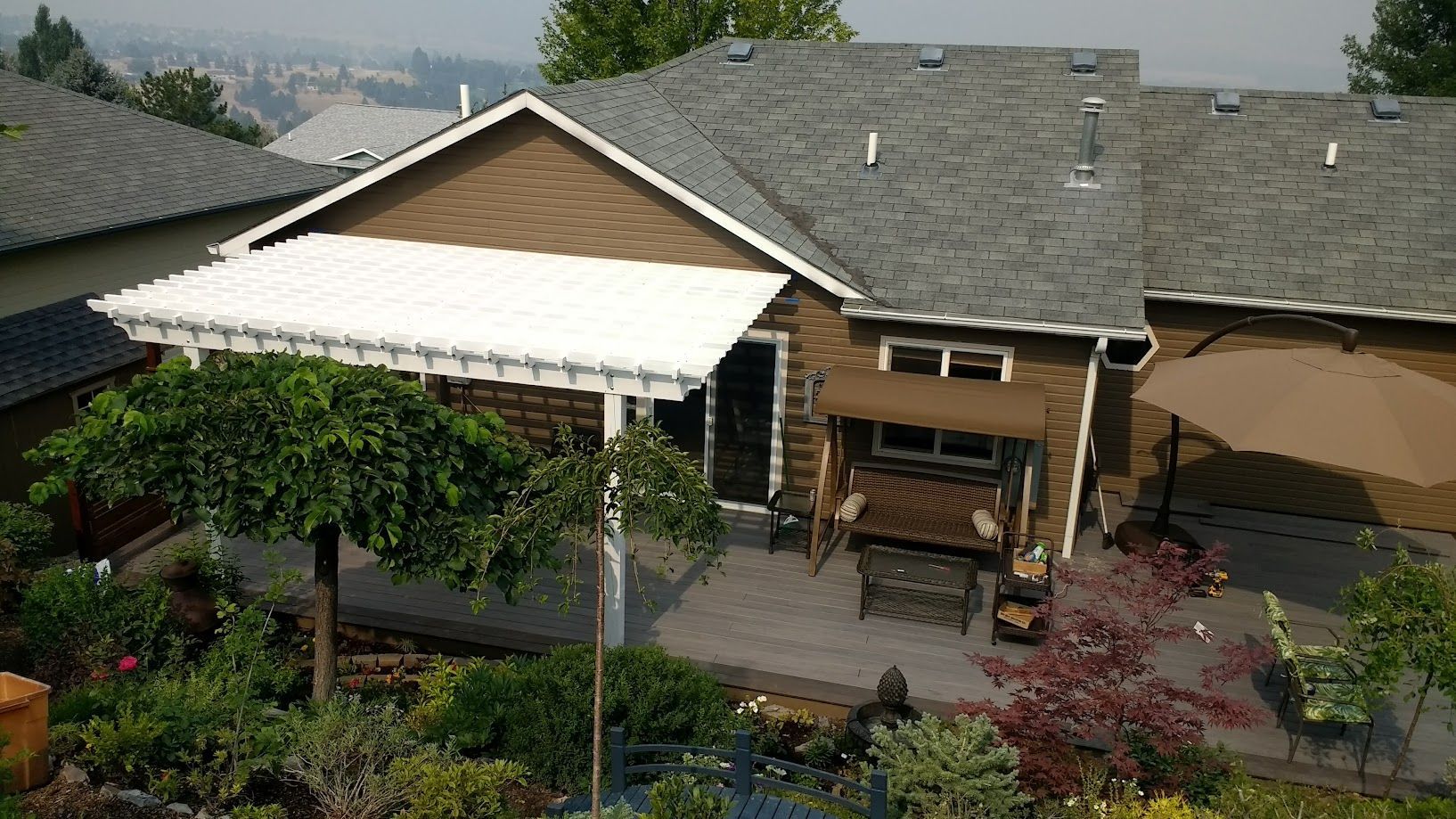 A tan house with a gray roof and white patio cover overlooking a lush, landscaped backyard with a patio set.