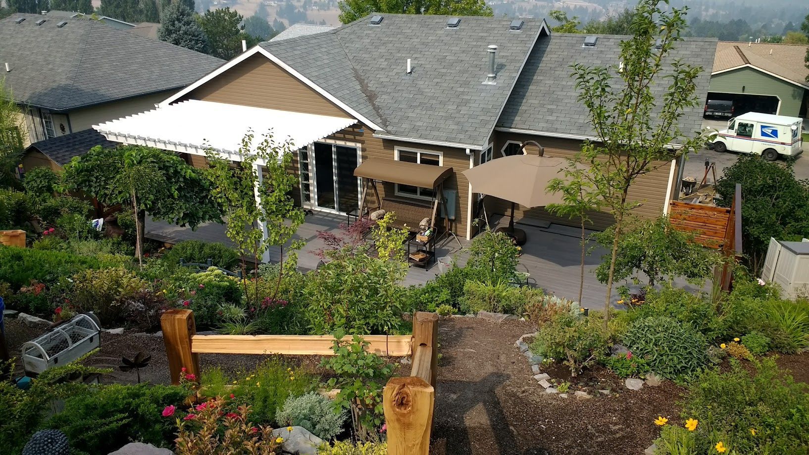 An elevated view of a house backyard with a white patio cover, a swing, patio furniture, and landscaped garden beds.