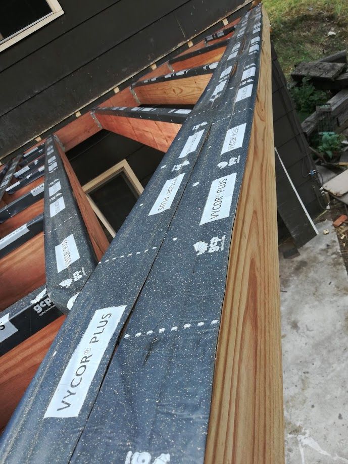Wooden deck joists and beams covered with black Vycor Plus flashing tape during construction.