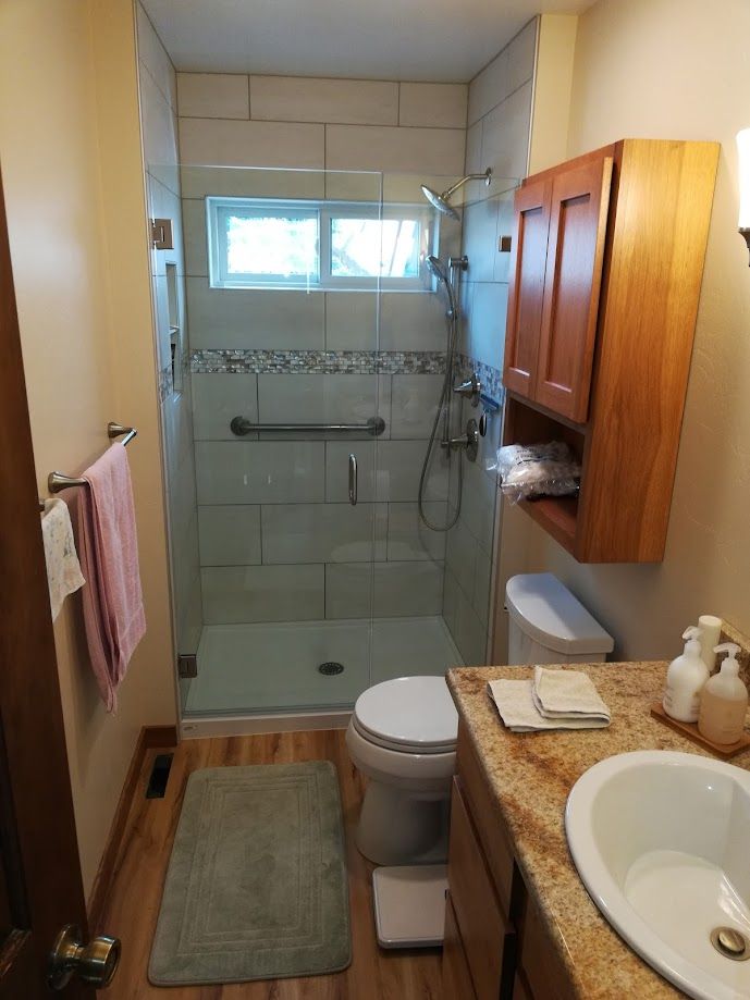 A bathroom with a tiled walk-in shower, a toilet, a wooden vanity with a stone countertop, and a wall-mounted cabinet.