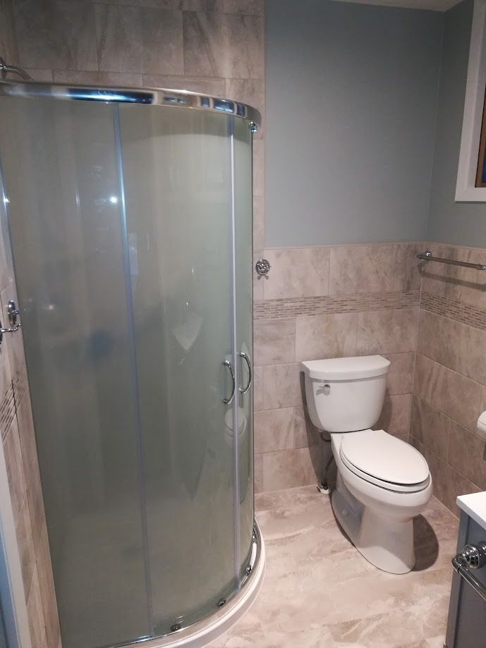 A corner shower with frosted glass doors next to a white toilet in a bathroom with beige tile walls and grey paint.