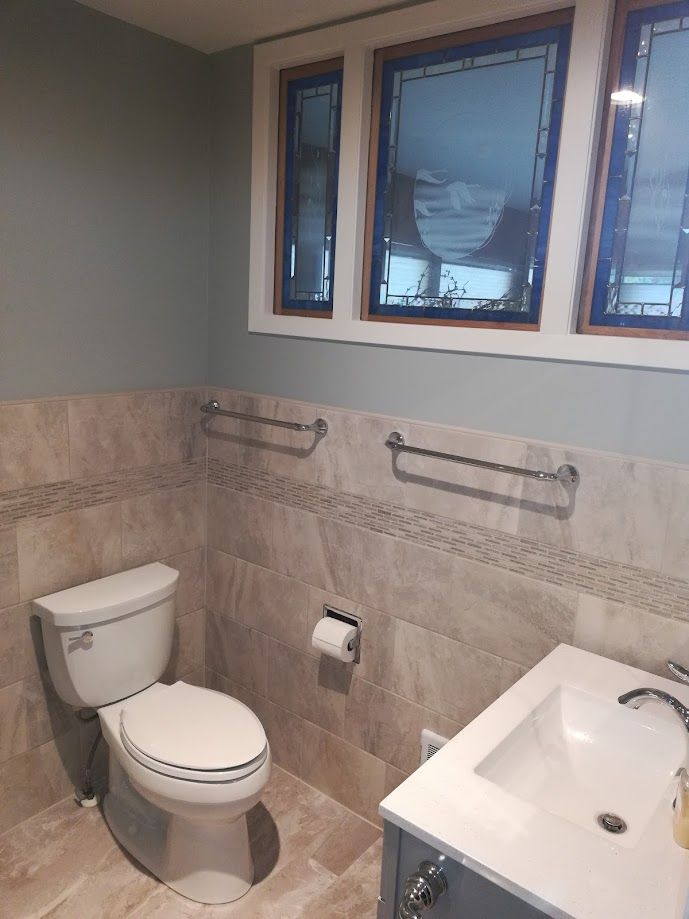 A bathroom with light gray walls, beige tiled walls, a white toilet, a modern vanity, and a three-pane window.