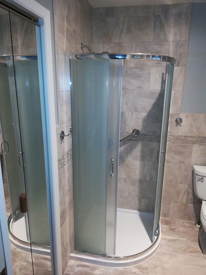 A curved glass shower enclosure with frosted panels, installed in a bathroom with light-toned tiled walls and flooring.