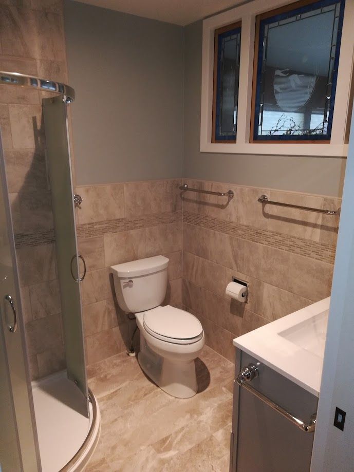 A modern bathroom with a glass-enclosed shower, beige tile walls, a white toilet, and a vanity with a white countertop.