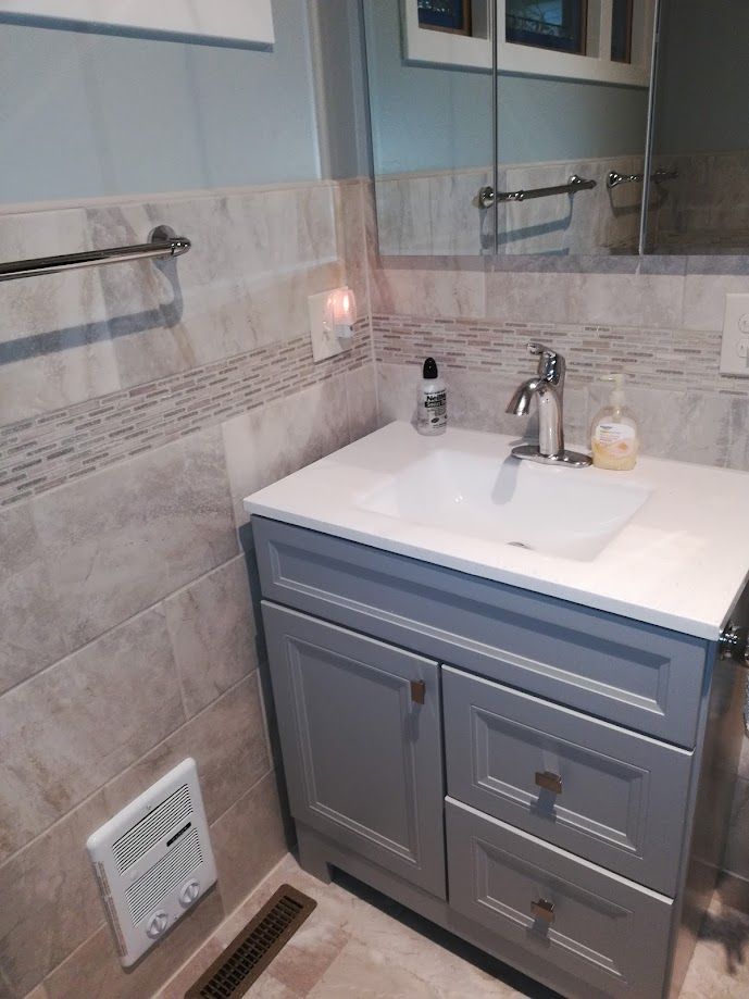 A bathroom vanity with a white countertop and sink, gray cabinets, beige wall tiles, a faucet, and a wall outlet.