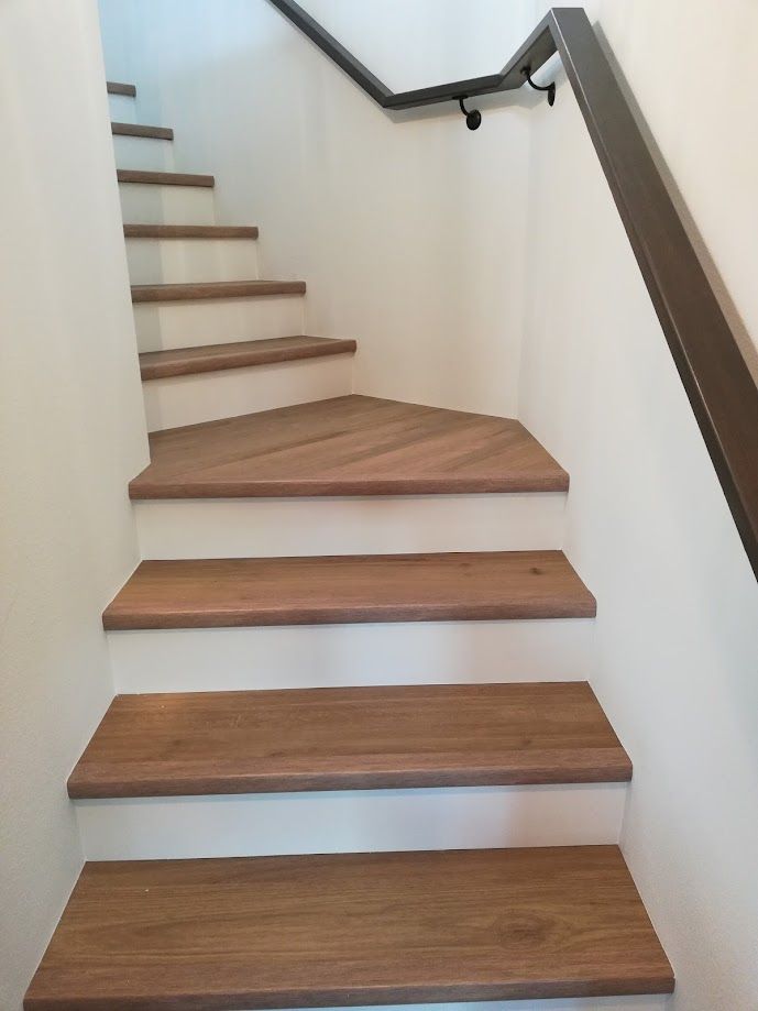 A staircase with wood-toned treads and white risers, featuring a dark handrail on a white wall.