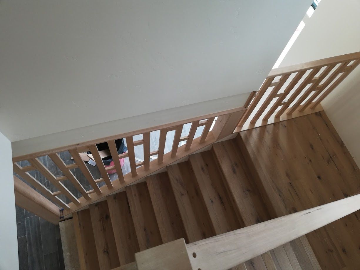 A high-angle view of wooden stairs with a matching railing, looking down toward a person standing at the bottom landing.
