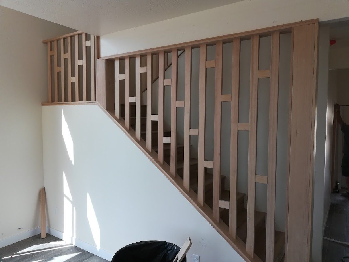 Wooden staircase railing with staggered vertical slats and a white wall, shown in a modern interior setting.