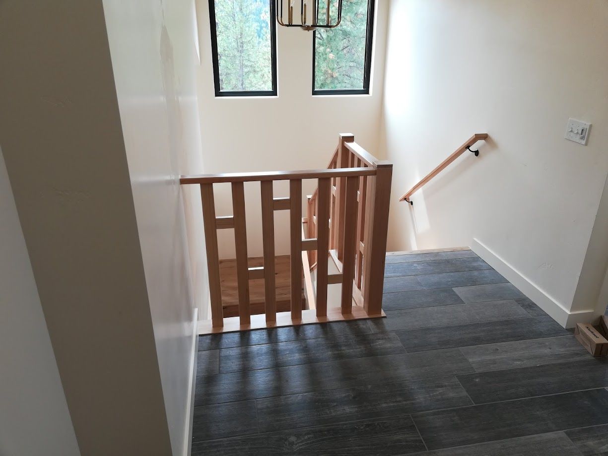 A staircase with a wooden railing and banister viewed from a landing with dark, textured square floor tiles.