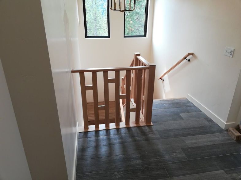 Staircase with a light wood balustrade and a matching handrail leading down to a landing with grey carpeted flooring.