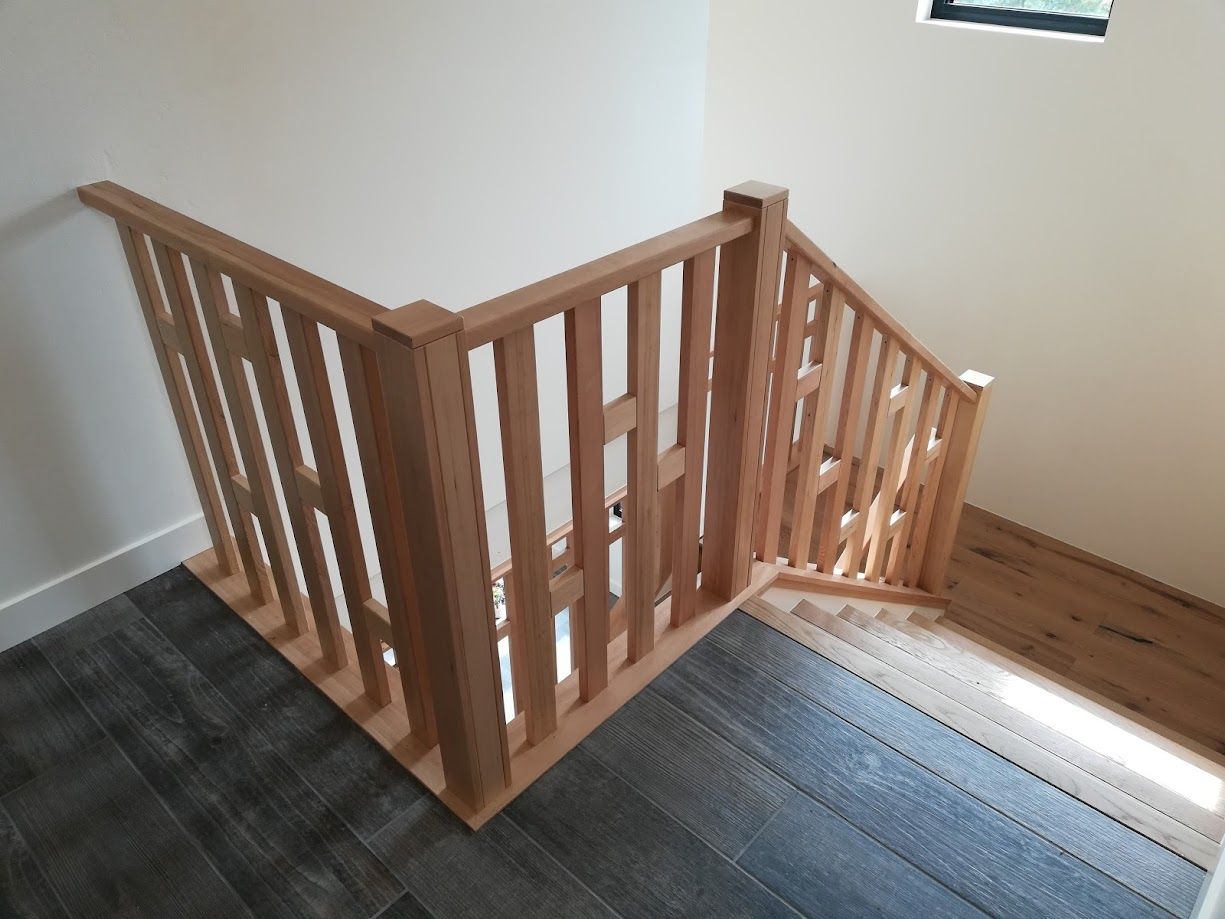 Modern wooden staircase railing with vertical balusters, separating a landing from the stairs in a bright, minimalist room.