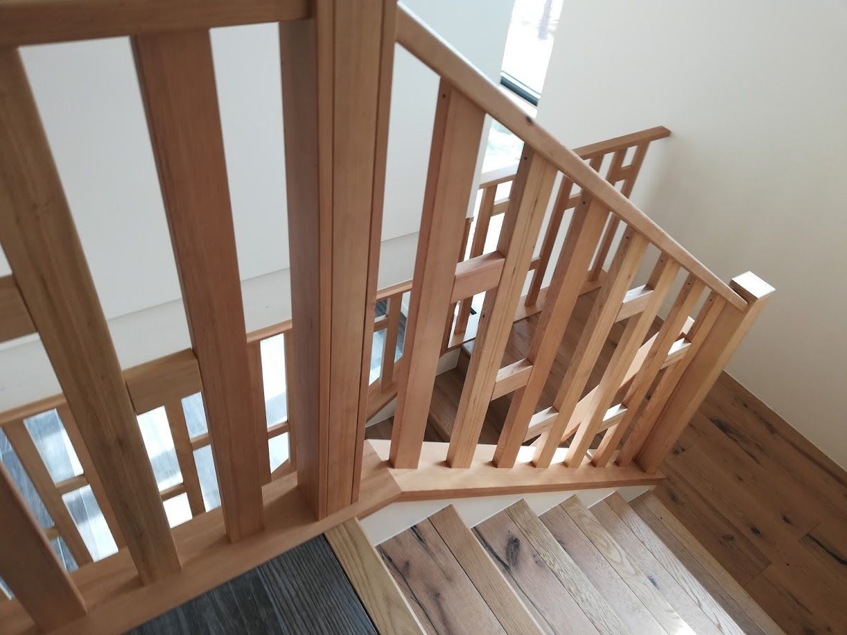 A light oak wooden staircase with vertical balusters and a matching handrail, seen from a high angle.