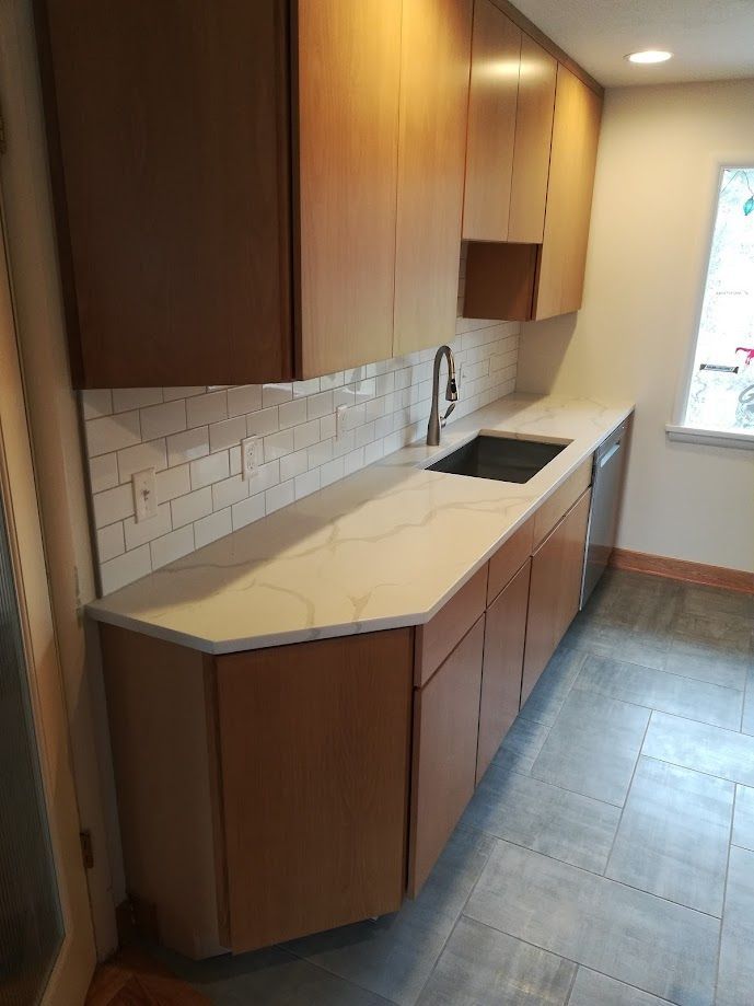 A kitchen view with wood cabinets, a white marble-look countertop, white subway tile backsplash, and a dark sink.