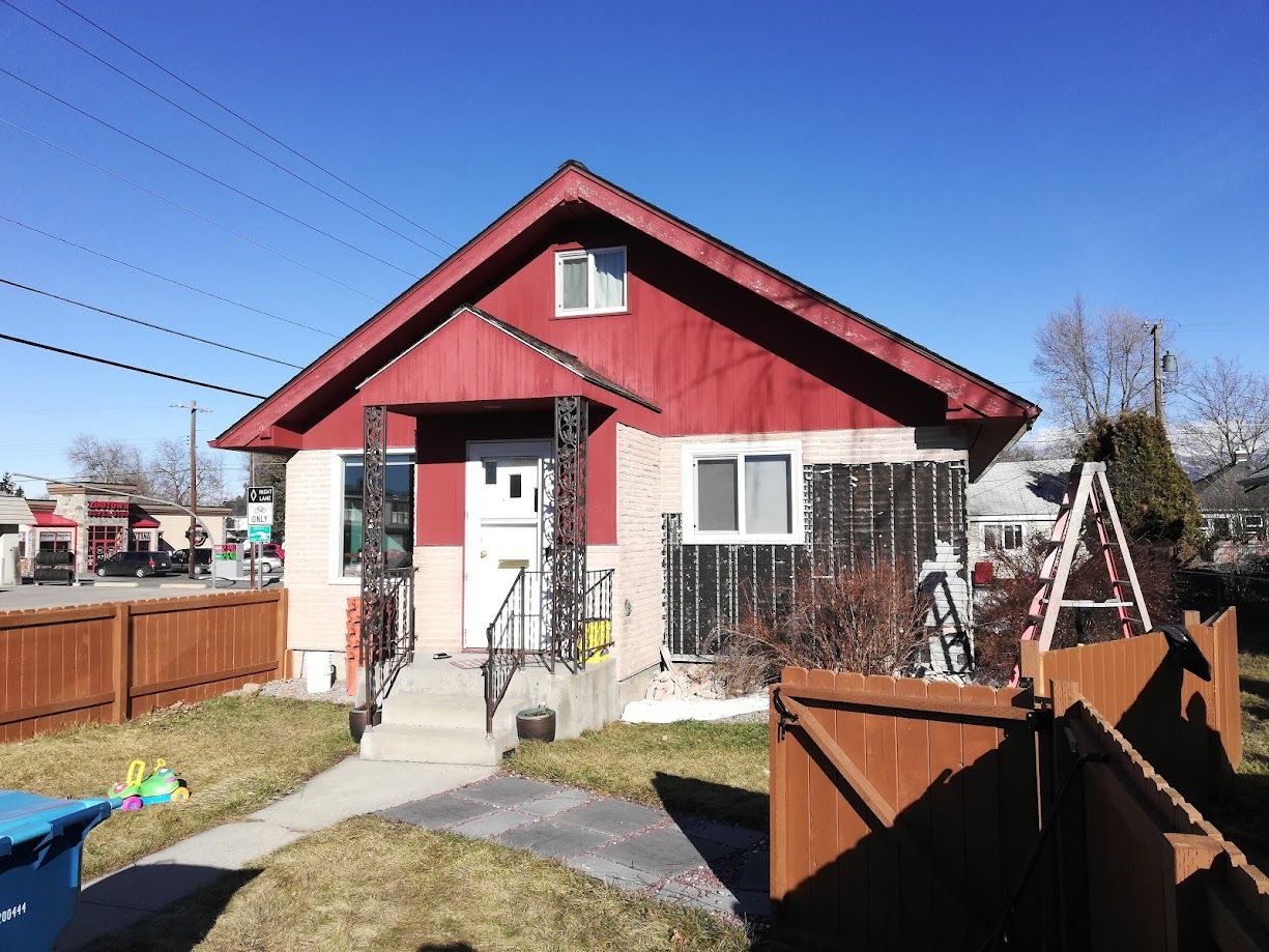 A one-story house with red upper siding and light lower walls, a front porch, a small yard, and a wooden fence.