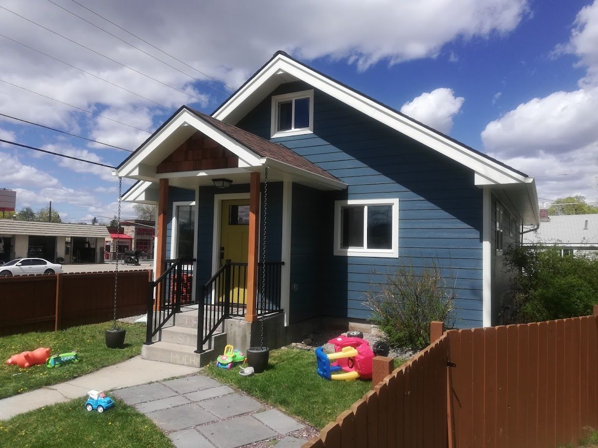 A blue one-story house with a white-trimmed yellow front door, a small front porch, and toys scattered on the front lawn.