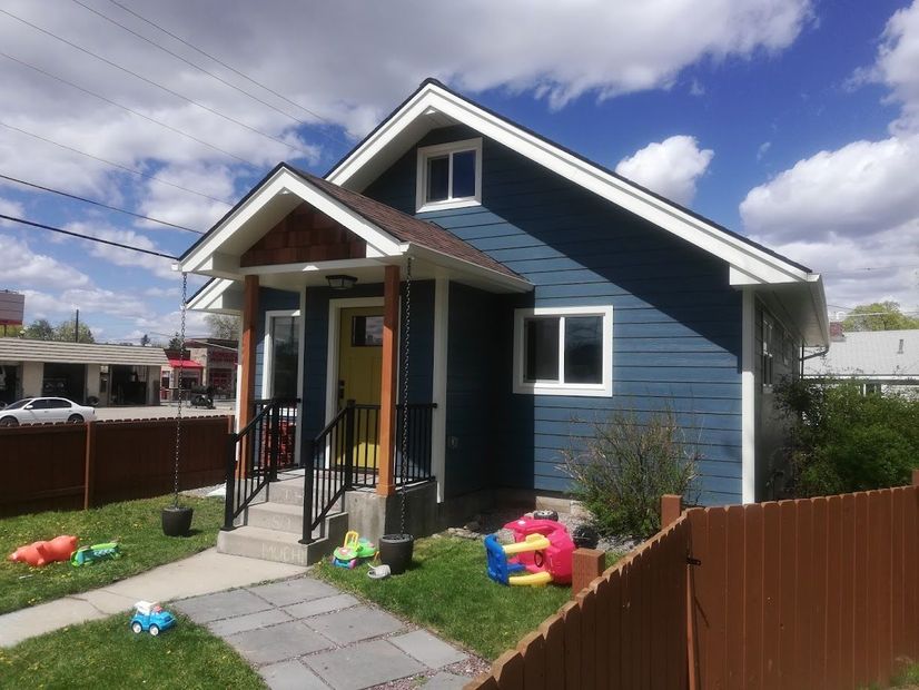 A blue house with a white-trimmed gabled entrance, yellow door, and a brown fence on a sunny day.