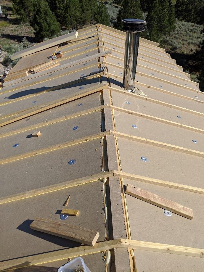 Roof insulation panels installed on a sloped roof with wooden rafters, metal fasteners, and a chimney stack.