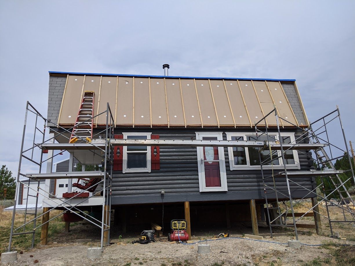 A cabin under construction with scaffolding around it, featuring new wooden panels installed on the roof.