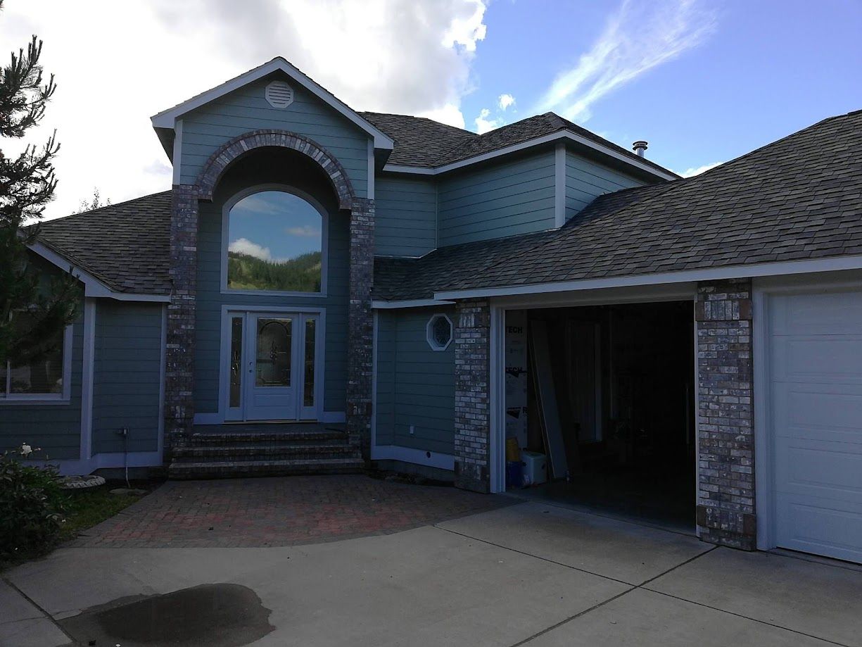 A two-story blue house with stone accents, a prominent arched entryway, and an open garage, under a bright sky.
