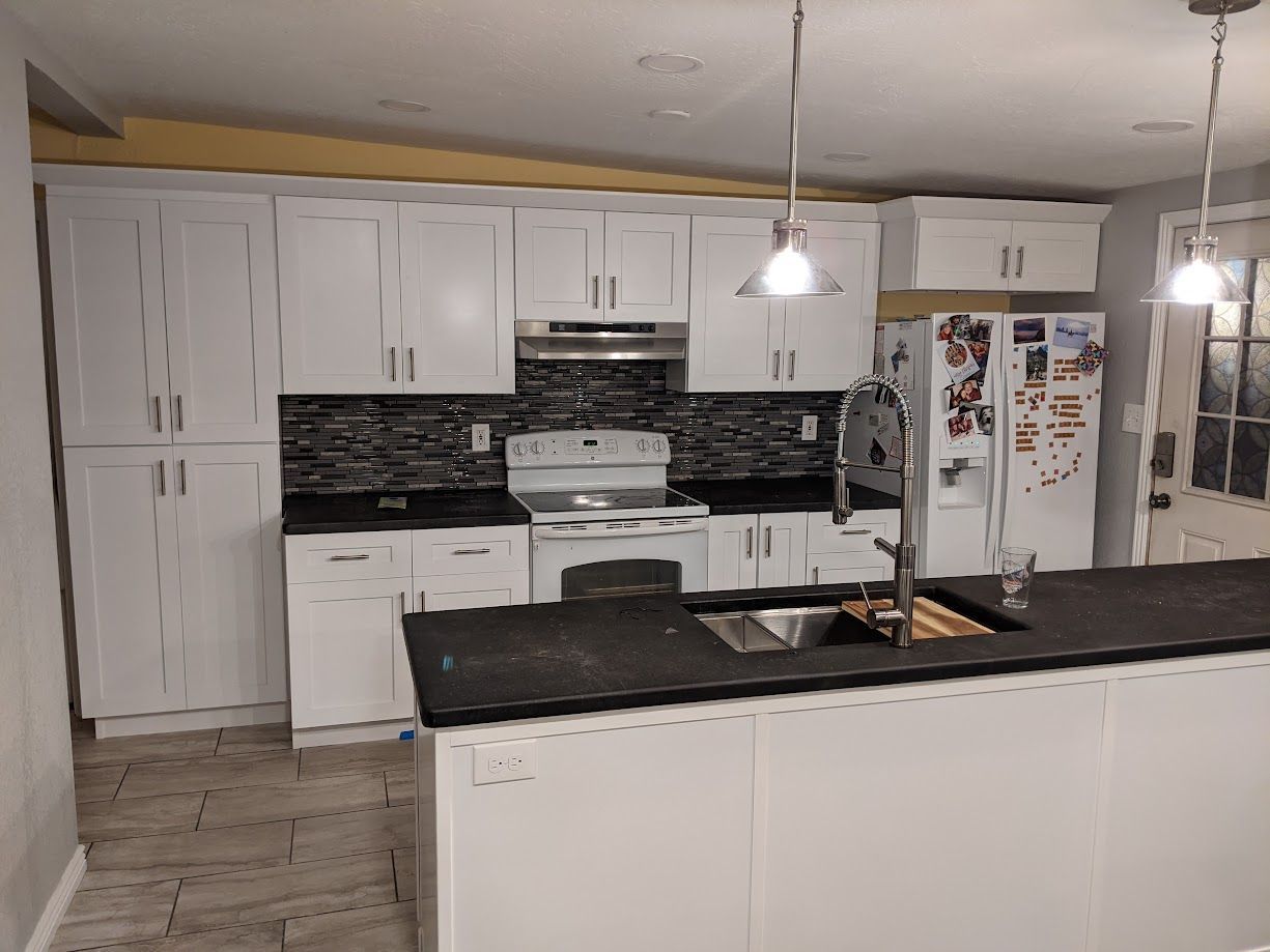 Modern kitchen with white cabinets, black countertops, a central island with a sink, and pendant lights.