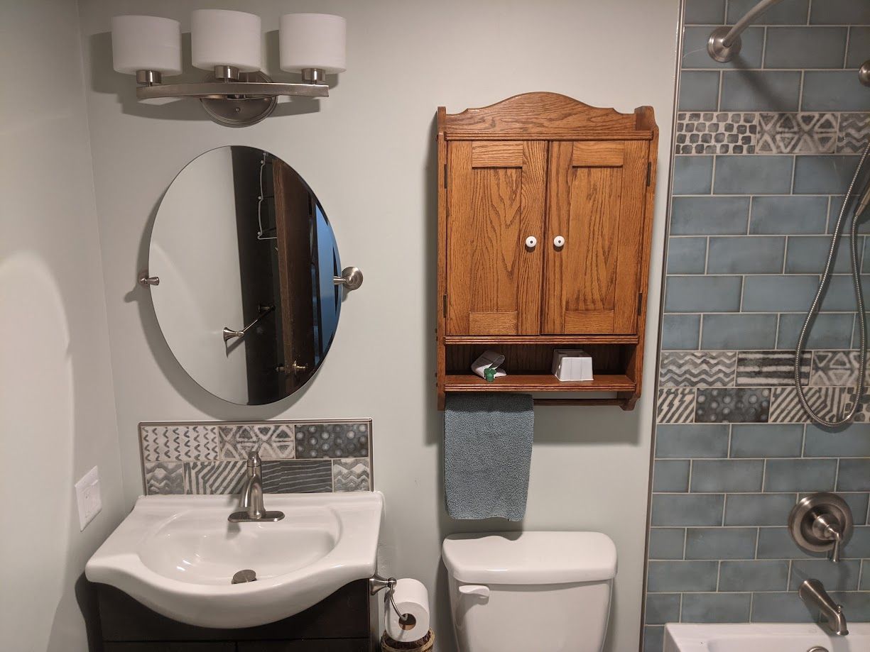 A bathroom vanity with a white sink, oval mirror, wall-mounted wooden cabinet, and blue subway tile shower wall.