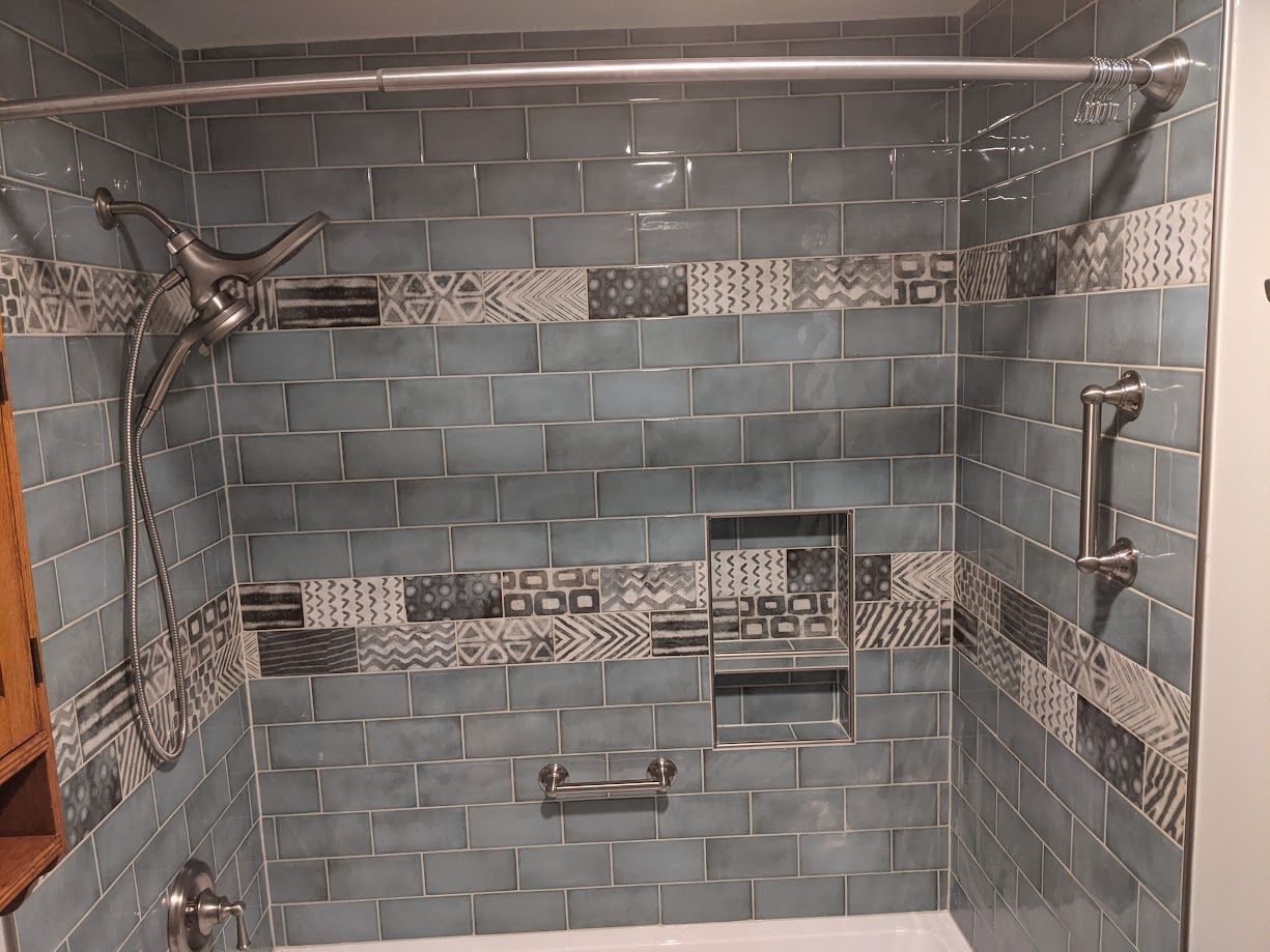 A blue-tiled bathtub shower with an accent border, a built-in wall niche, chrome shower hardware, and grab bars.