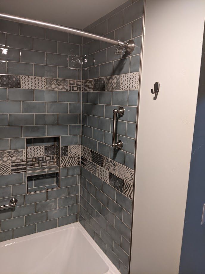 A bathtub shower with blue subway tiles, a decorative patterned border, built-in recessed shelves, and a safety grab bar.