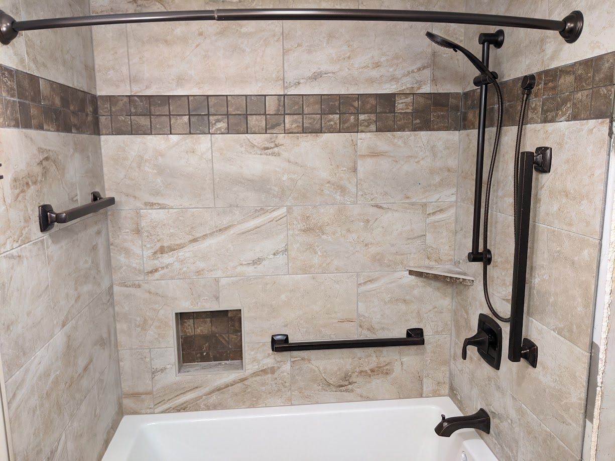 Bathtub and shower with tiled walls, bronze hardware, and multiple safety grab bars installed.