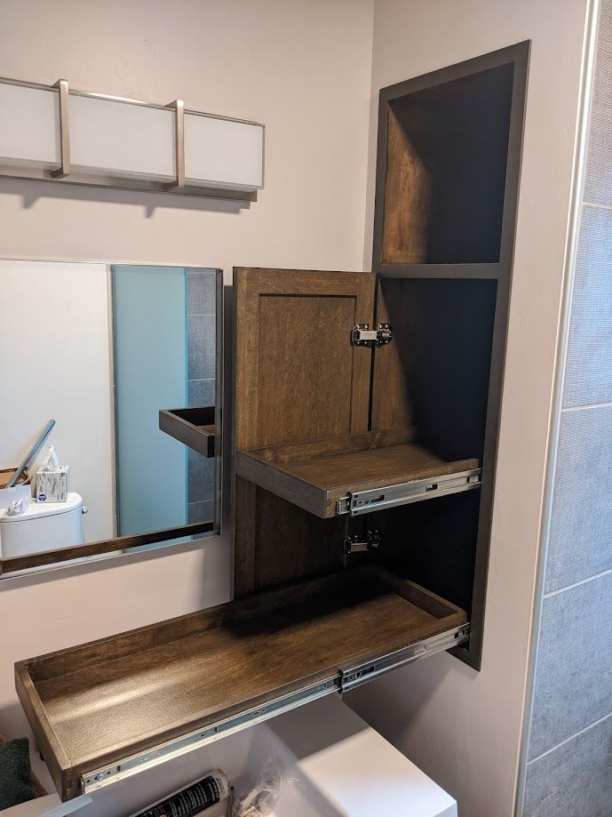 A built-in bathroom wall cabinet with two shelves extended outward on sliding tracks next to a vanity mirror and light.
