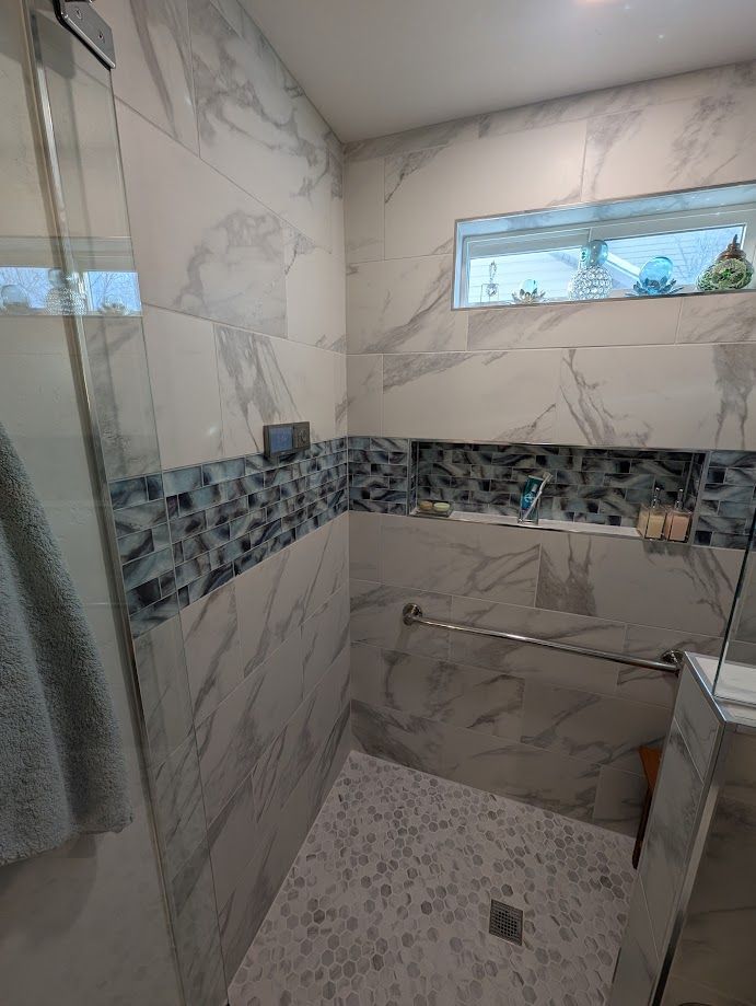A walk-in shower with white marble-look walls, a blue glass tile accent strip, a small window, and a silver grab bar.