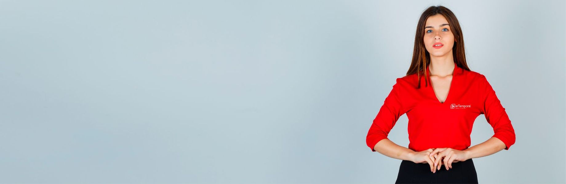 Una mujer con una camisa roja y pantalones negros está de pie con las manos en las caderas.