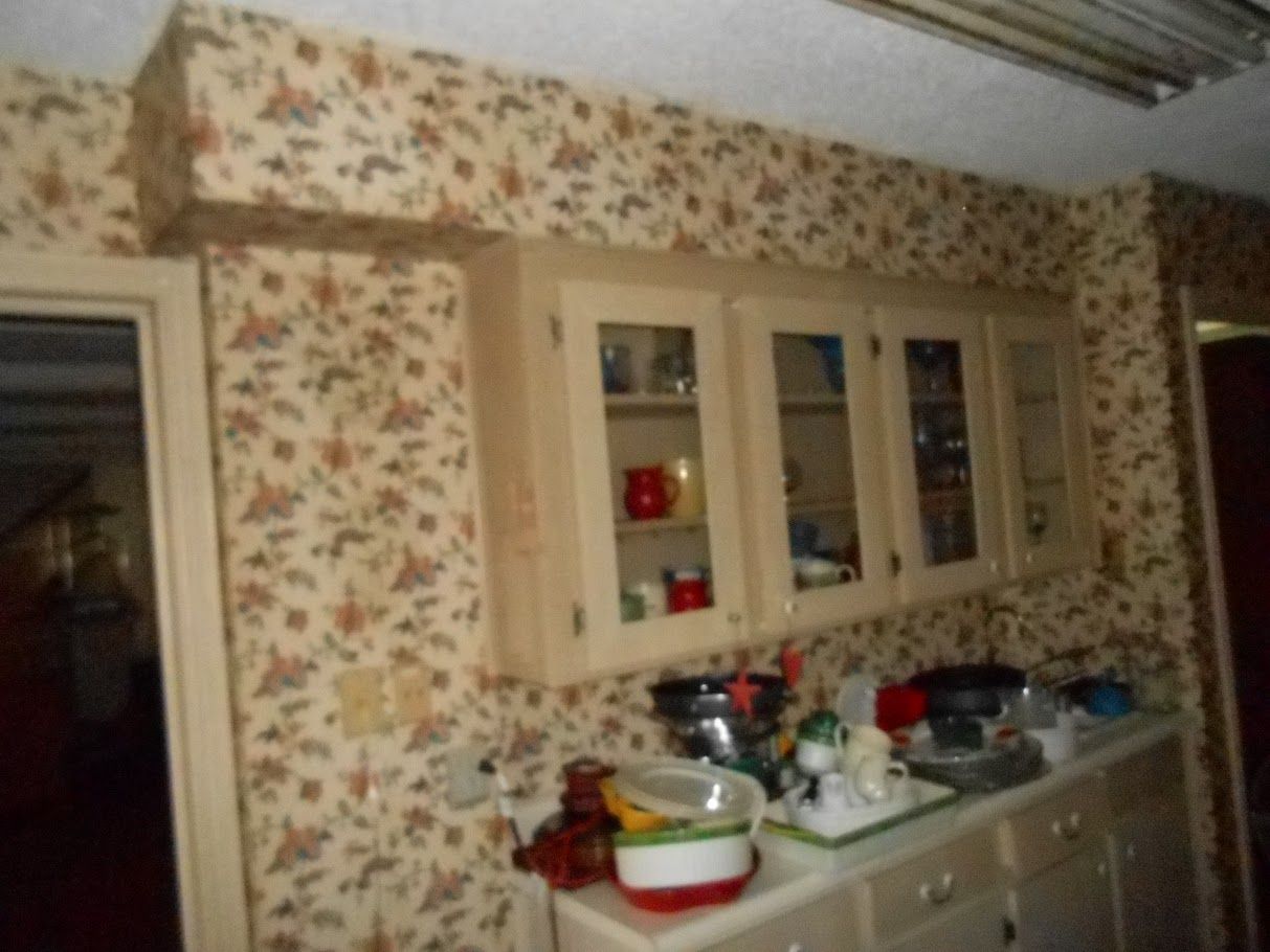 A kitchen with a floral wallpaper and white cabinets