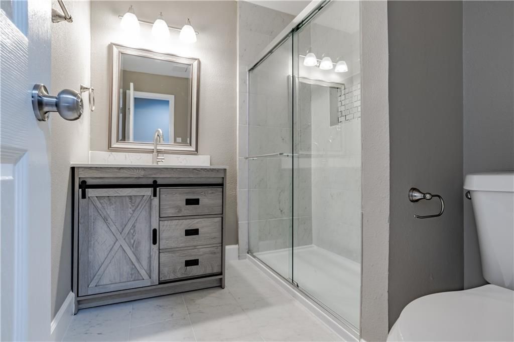 A bathroom with a toilet, sink, mirror , and walk-in shower.