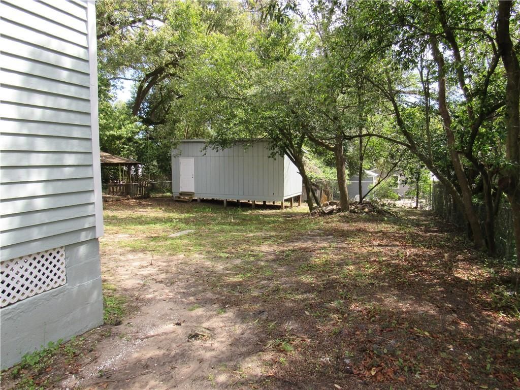A white house with a shed in the backyard surrounded by trees.