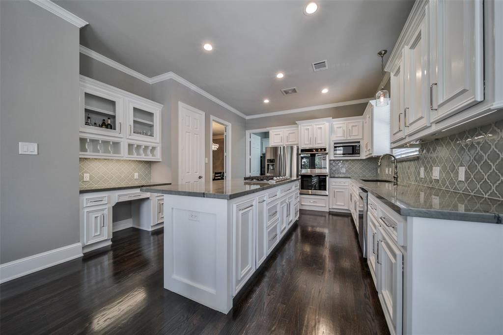 A kitchen with white cabinets, granite counter tops, and hardwood floors.
