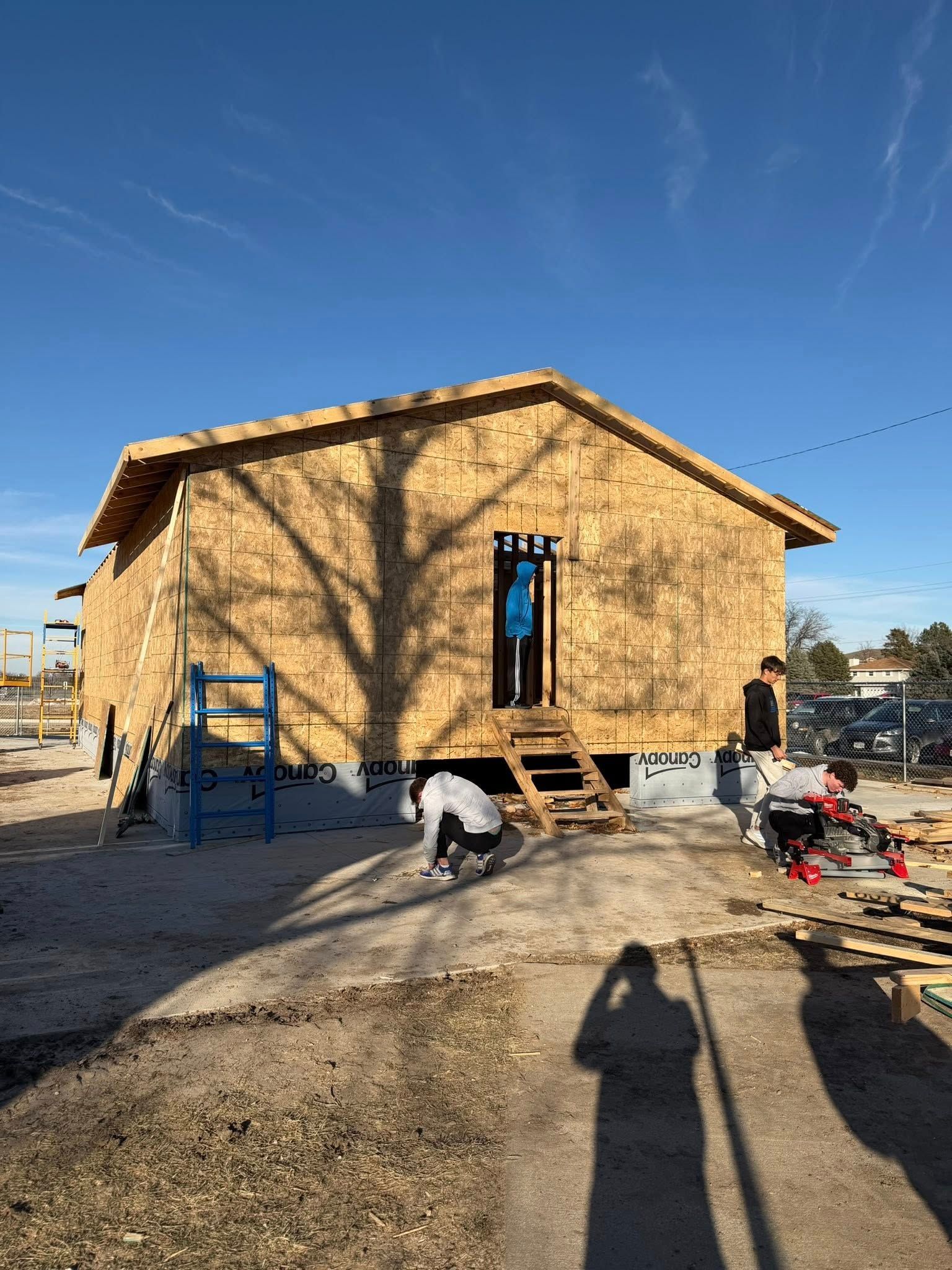 Volunteers work on the plywood exterior of a small house under construction on a sunny day.