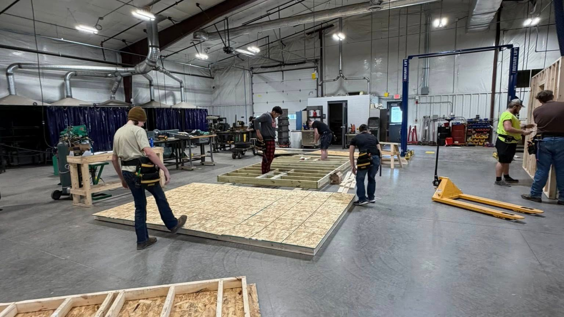 Construction workers build a wall section in a workshop.