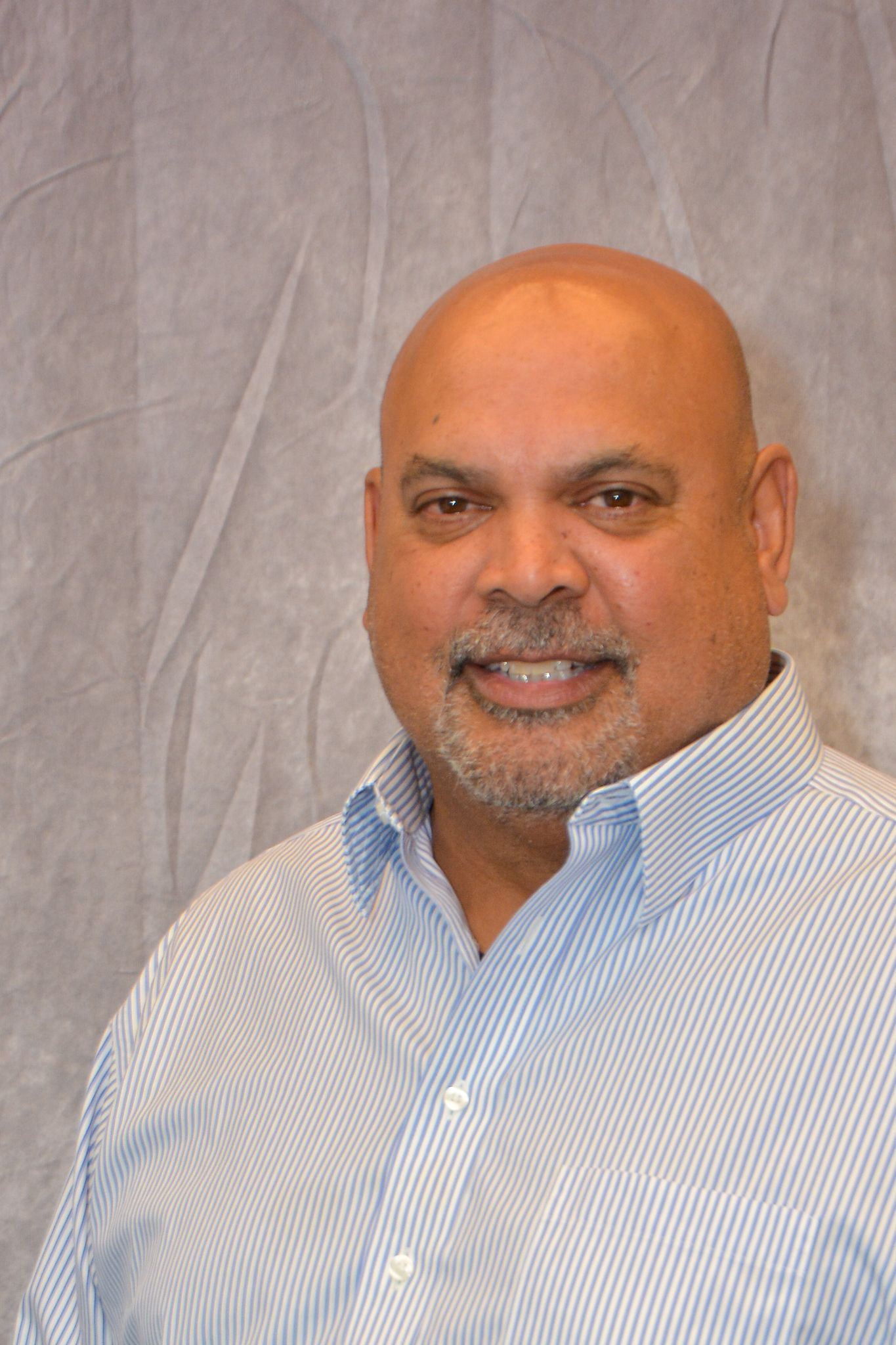 A headshot of a man with a goatee wearing a blue First Citizens Bank quarter-zip fleece against a light gray background.
