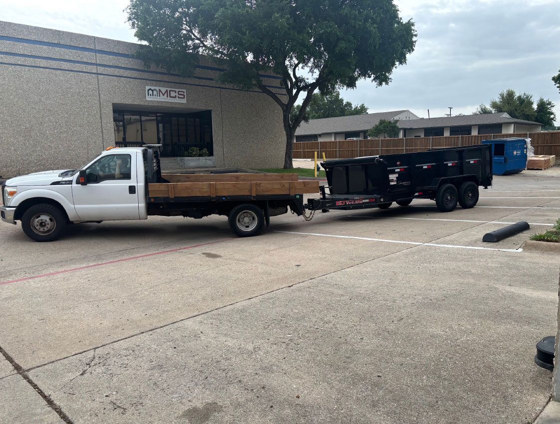 White pickup with flatbed trailer parked beside a brick building in a lot