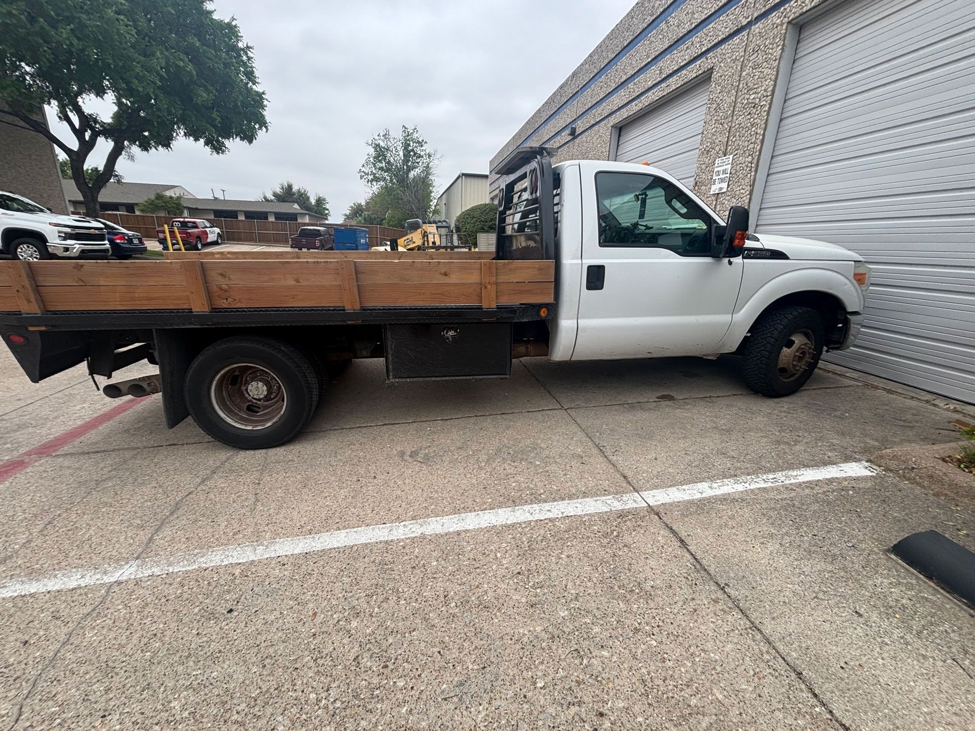 White flatbed pickup truck parked beside a building on a concrete lot