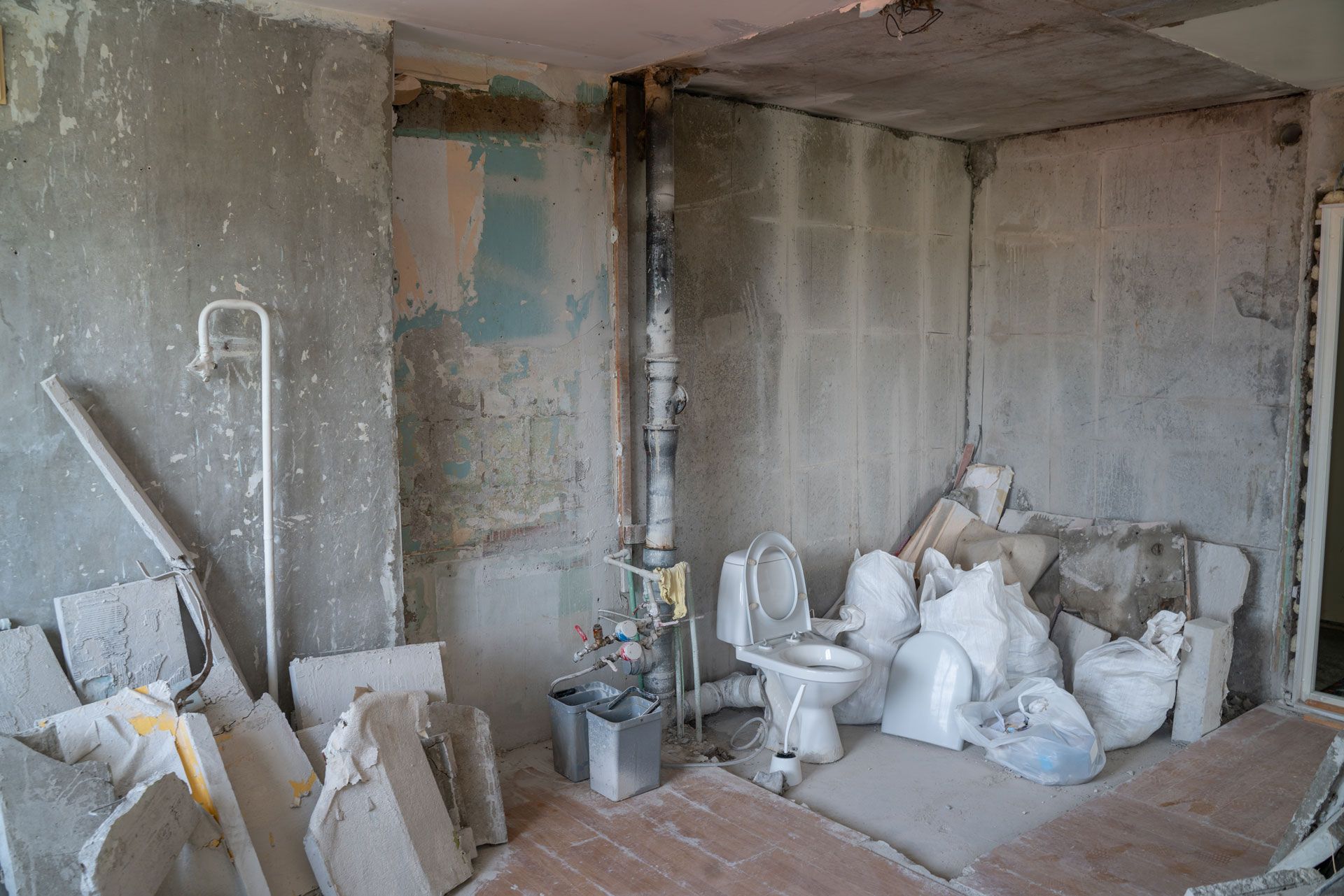 Dusty unfinished room with exposed pipes, plaster debris, and bags of construction material on the floor