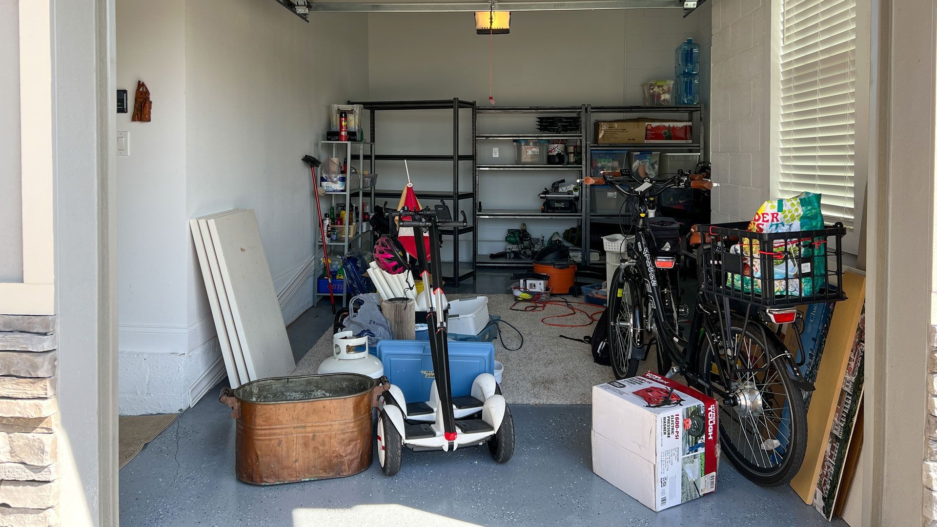 Cluttered garage with shelves, bicycles, a stroller, and boxes stored along the walls