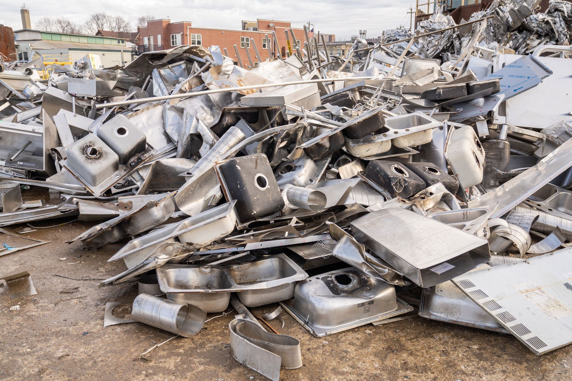 Pile of broken white kitchen sinks and debris in a muddy demolition site near houses