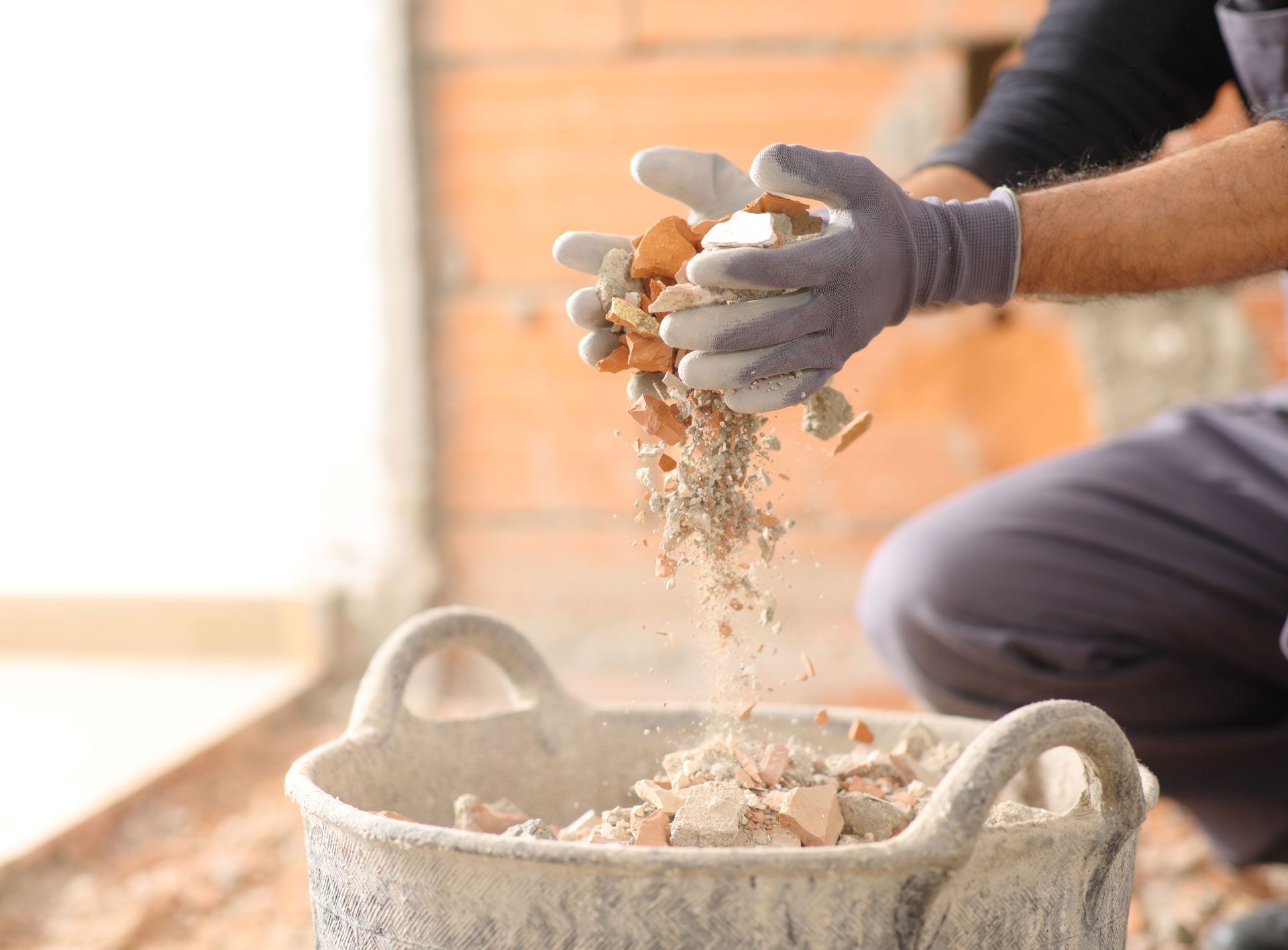 Gloved hands sifting sand into a bucket at a construction site