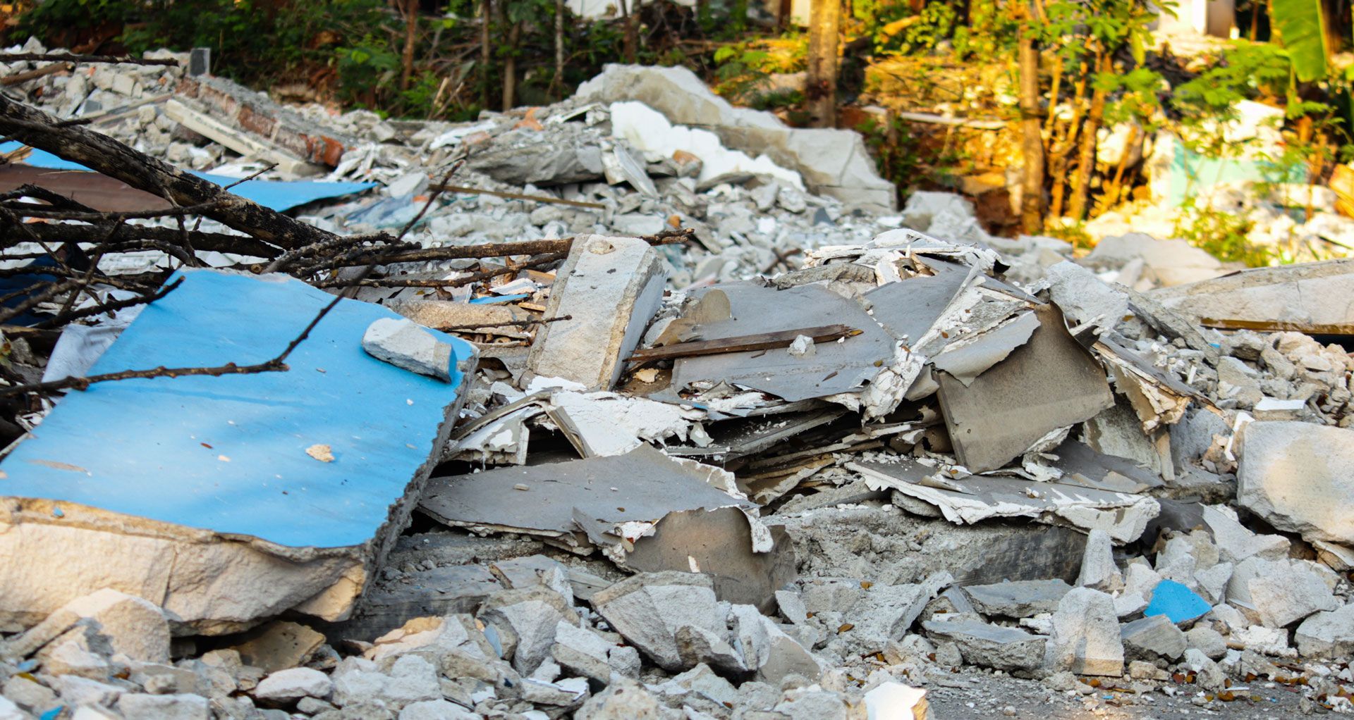 Collapsed building rubble with broken concrete slabs and debris, including a blue panel, in an outdoor area.