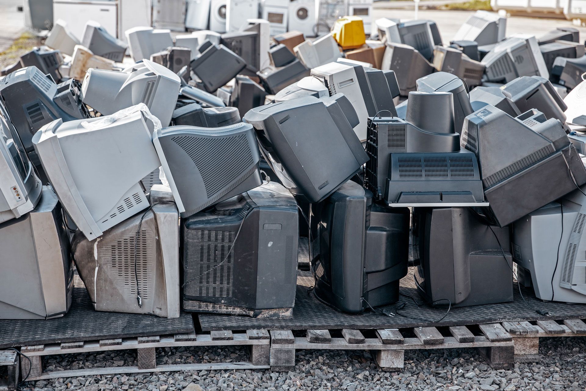 Pile of discarded old computer monitors and electronics stacked on wooden pallets outdoors